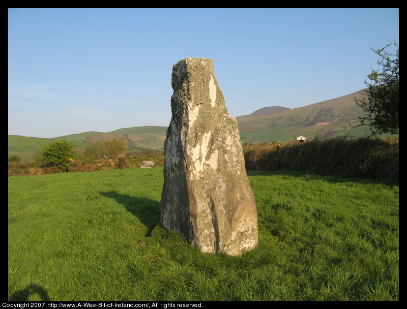 standing stone in a green pasture near stone walls that are much more recent with mountains in the background.