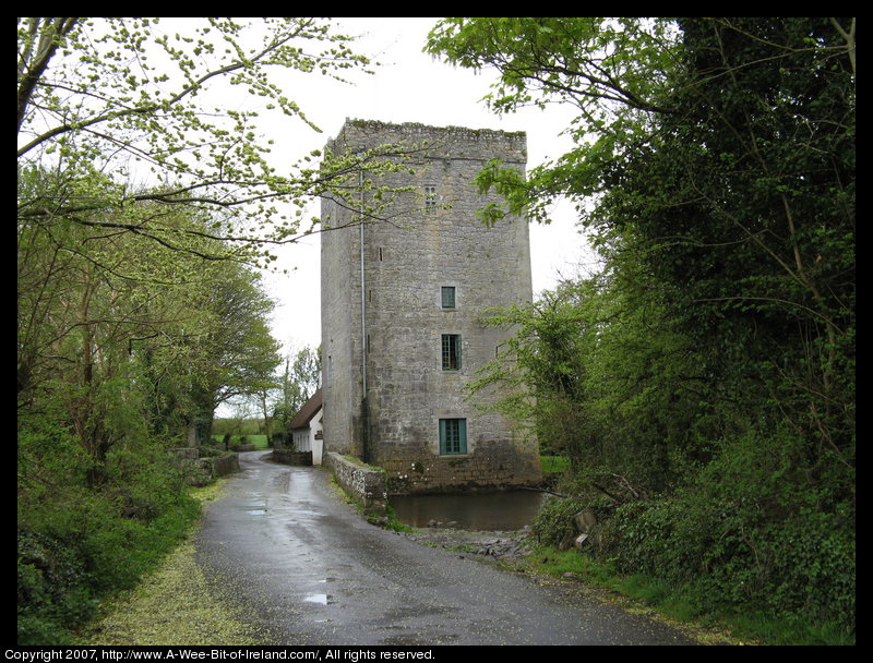 A 14th century Norman tower house that was the residence of William Butler Yeats stands next to a stream surrounded by tall trees.