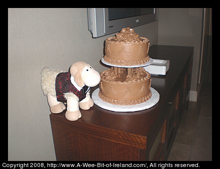 Curious Sheep is a stuffed toy sheep. Curious Sheep is next to a cake.