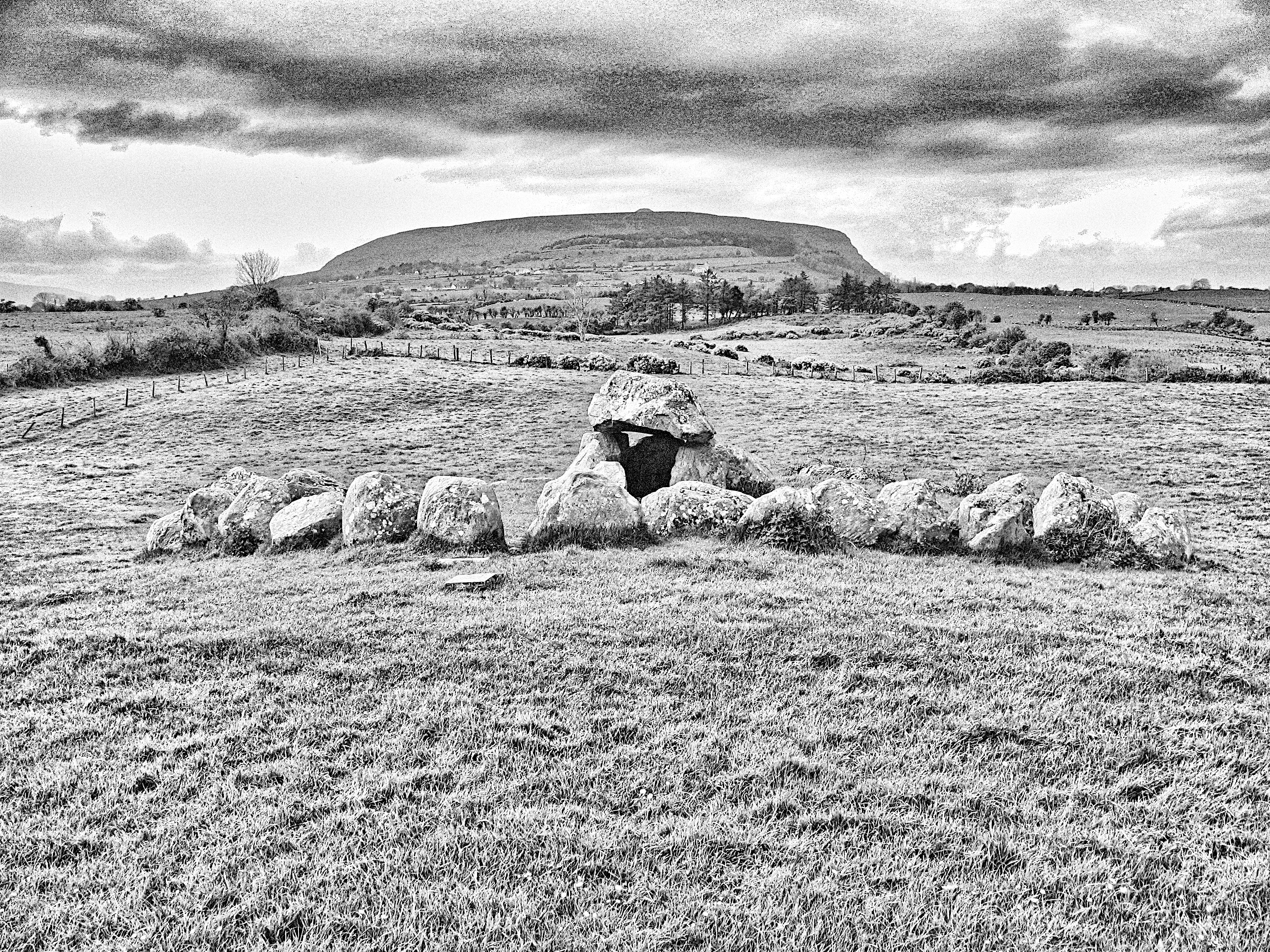Two structures of very large stones that were once part of a burial complex built 5000 or 6000 years ago. In the background is a mountain with a cairn at the top.