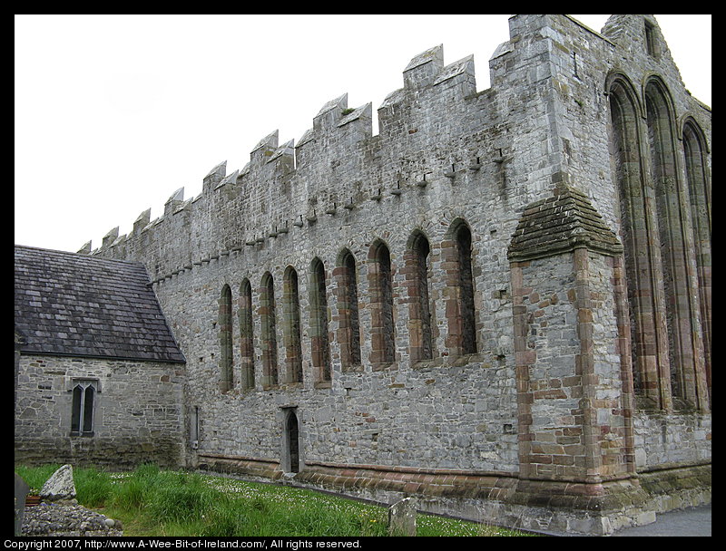 A ruined cathedral built of stone. There is no roof. There are tall narrow openings for windows in the walls.