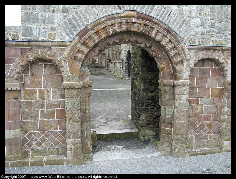 A ruined cathedral built of stone. There is no roof. There are arches made of carved stone that has red color.