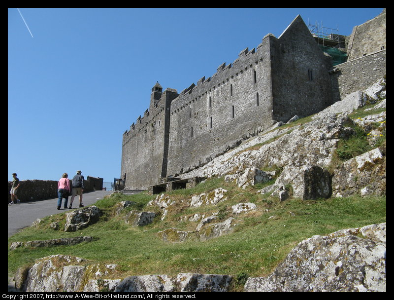 There is a paved road leading up to a gate in a high stone wall. This is on a rocky hill with a tall former church building that is now a museum.