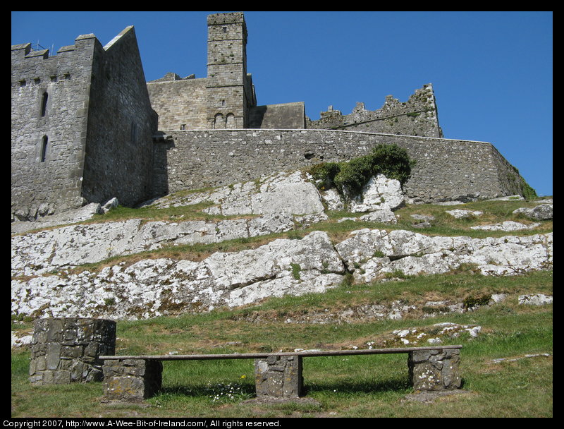 There is a steep rocky hill with a high stone wall and ruins.
