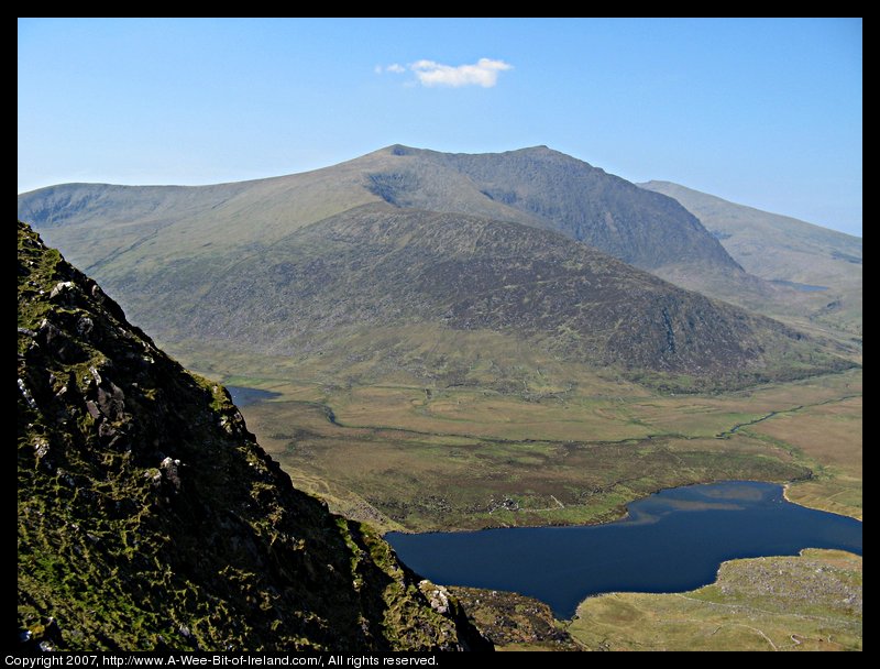 Standing on the edge of a very steep mountain looking at a lake about 300 meters below and another mountain beyond the lake.