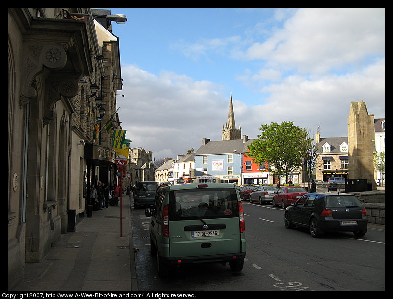 There is a paved triangular area with places to sit and a tree and shops.