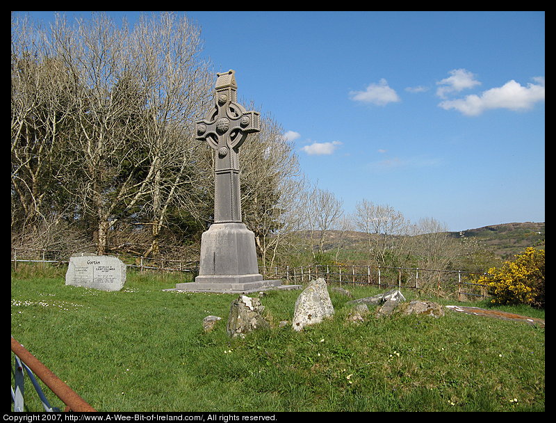 A tall Celtic Cross in a fenced of area that also contains a megalitic stone monument.