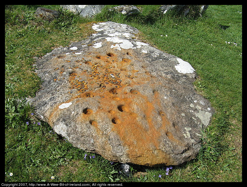 A fallen stone monument. One large stones has many cups carved into it as was common for megalithic monuments. There are coins placed on the stone.