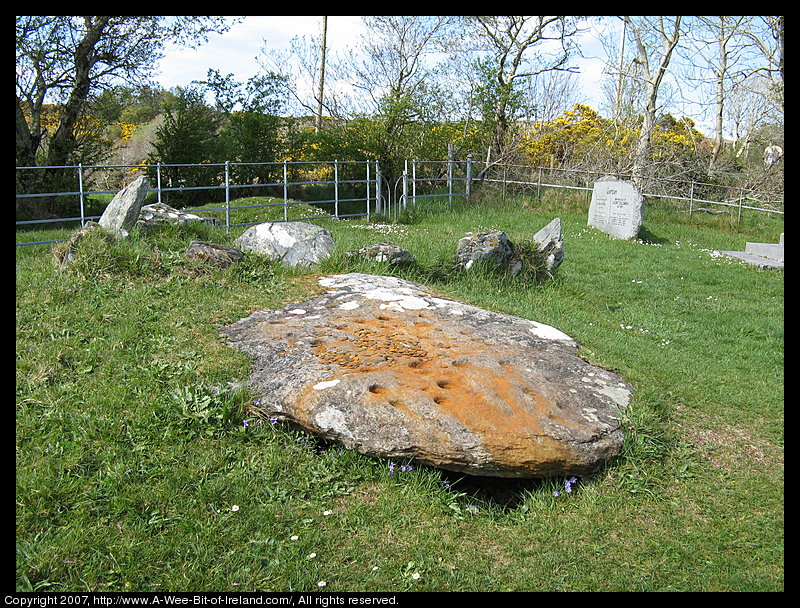 A fallen stone monument. One large stones has many cups carved into it as was common for megalithic monuments. There are coins placed on the stone.