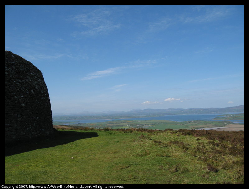 A tall curved stone wall on the left with Lough Swilly and mountains in the background.