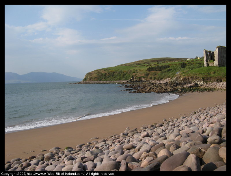 A ruined castle next to the ocean and a beach of smooth boulders.