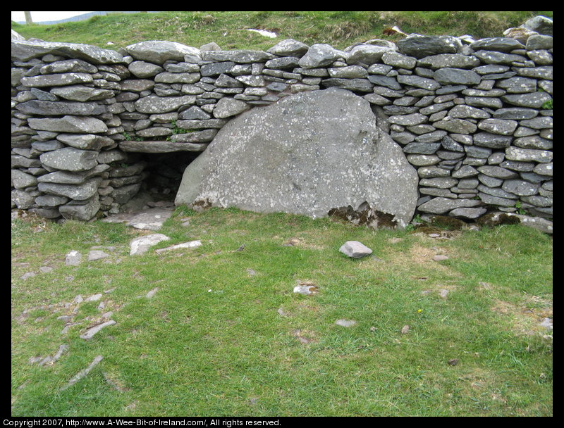 There is a large stone slab next to a small opening in a stone wall.