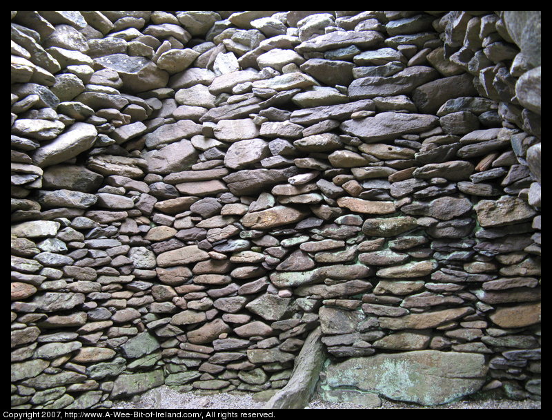 A stone wall and part of the stone roof of a clochan seen from the inside.