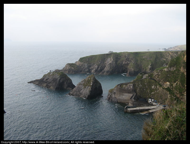 A steep narrow road winds down a cliff to a concrete and stone pier.