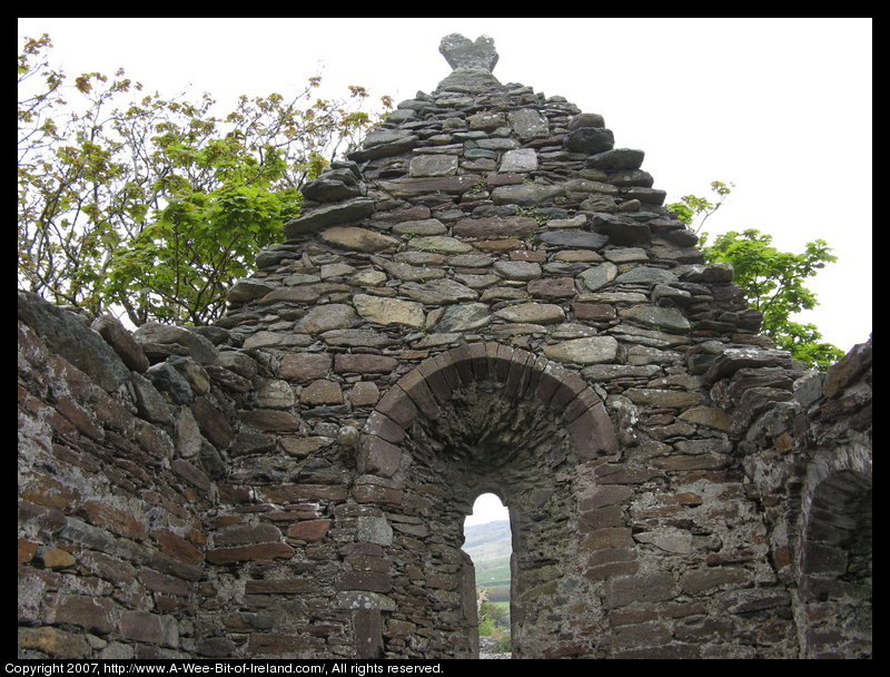 A stone arch window in the ruin of a church.