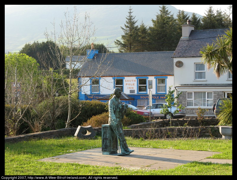 A sculpture of Tom Crean holding two puppies with the South Pole Inn in the background across the street. Annascaul, Kerry, Ireland.