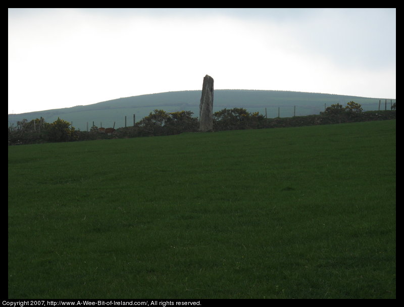 standing stone in a green pasture near stone walls that are much more recent with mountains in the background.