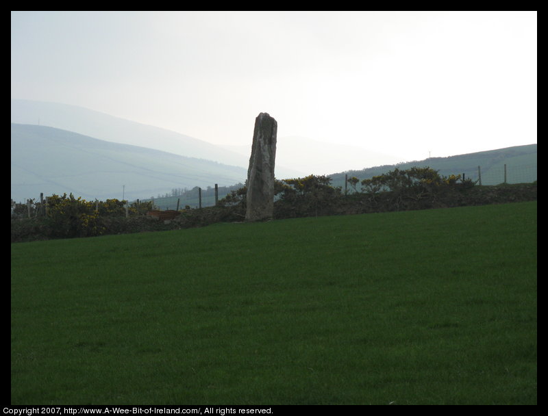 standing stone in a green pasture near stone walls that are much more recent with mountains in the background.