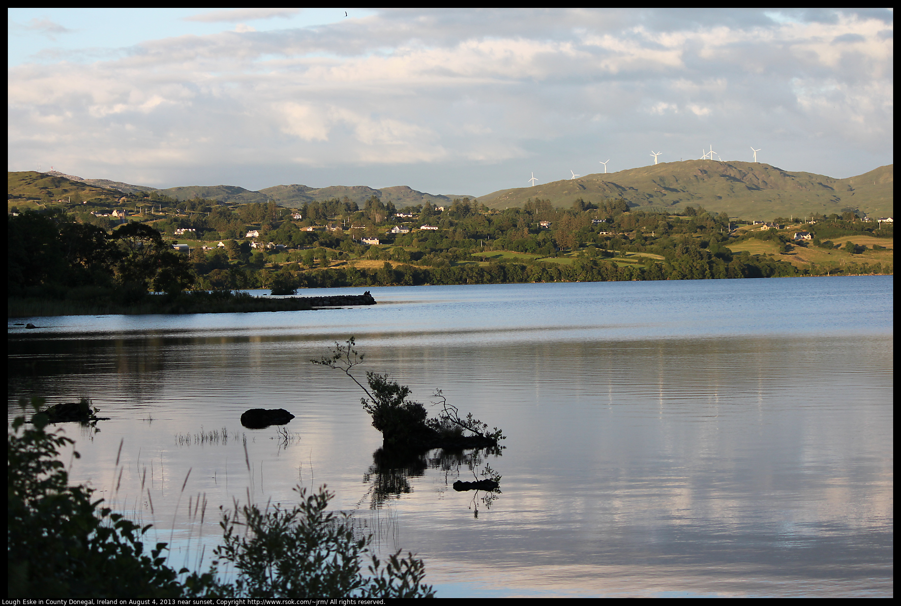 A lake in the shadow of a mountain with the far side of the lake still lit by sunlight.