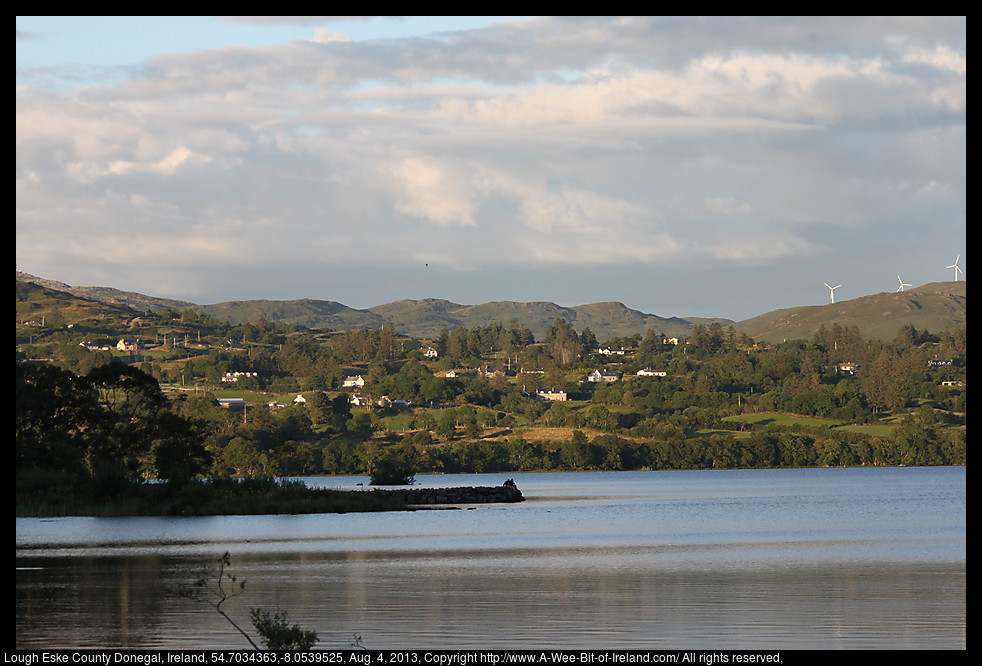 A lake in the shadow of a mountain with the far side of the lake still lit by sunlight.