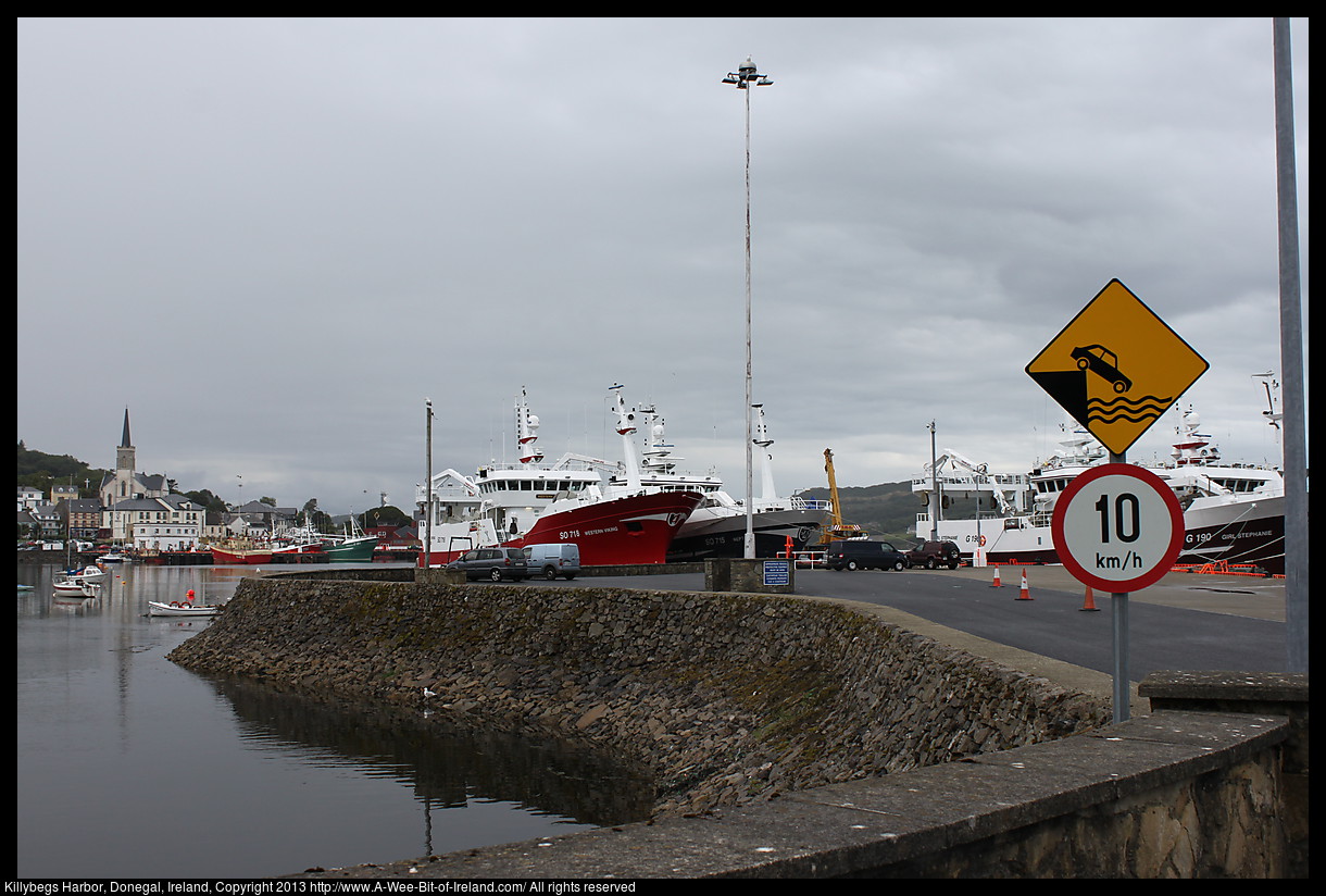 A harbor with various sizes of boats and ships and cars parked on the pier.