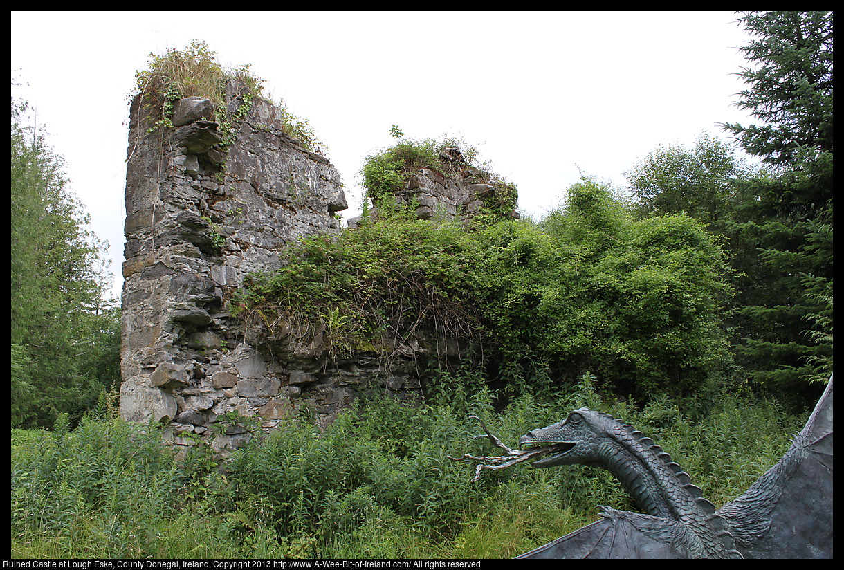 A sculpture by Lloyd Le Blanc of a dragon before a ruined stone castle wall.