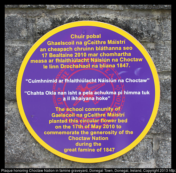 A plaque on a stone wall with writing in 3 languages. In English it says it commemorates the generosity of the Choctaw Nation for their generosity during the great famine of 1847