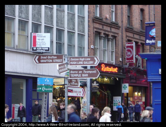 A street in Dublin. There are steet signs pointing the way to Grafton Street, Temple Bar, Hugh Lane Gallery and Dublin Tourism Centre.