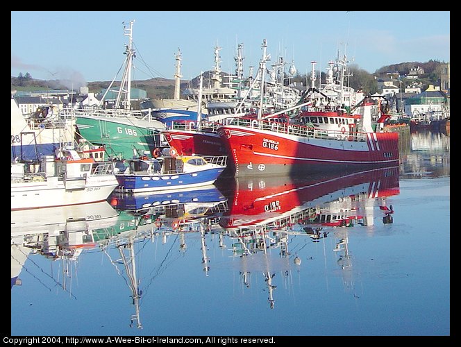 Fishing Fleet at Killybegs. The sun is shining brightly. The harbor is
so still that it is like a mirror reflecting the brightly colored ships. 
There is smoke rising from a chimney and scattered clouds.