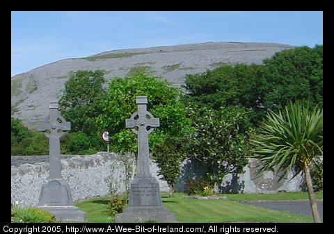 Looking across a church yard at the Burren in County Clare Ireland.
      There are two Celtic Cross grave stones in the foreground with the
      rocky hills of the Burren in the background.