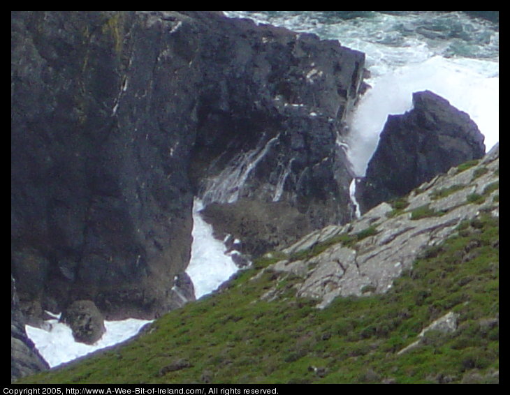 Waves crashing on rocks beneath cliffs and spilling over the rocks.