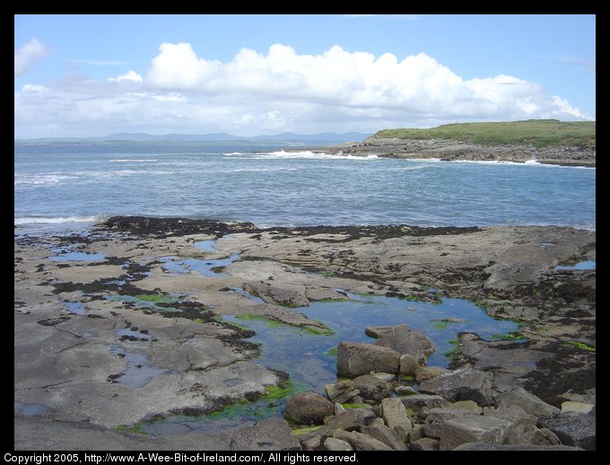 Tidal pools and surf at Creevy in County Donegal. It is low tide and
 the Blue Stack Mountains are on the horizon across Donegal Bay. There is
 no sandy beach here, just rocks and pools of water.