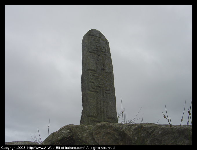 Slab of stone with a crosses incised. It is on a rocky outcrop.