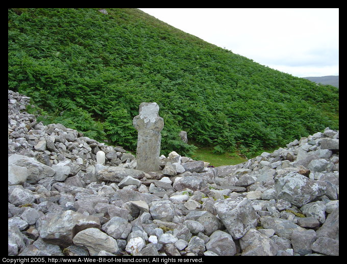 A mound of gray stones on a mountain side with a stone cross.