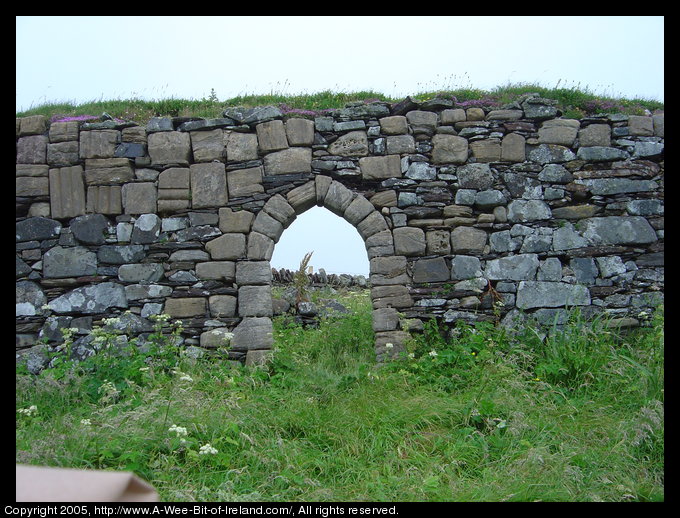 Ruins of a church Inishkeel Island near Naran, Donegal
 There is a view of sky and stone fence through a stone arch.