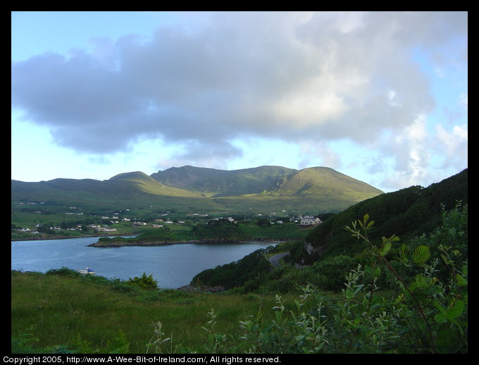 View Across Bay of Teelin, Donegal. Teelin Village is across Teelin
Bay. There is sunshine on the mountain behind Teelin Village. The slope
down to the bay is Irish green and the water of the bay is blue.